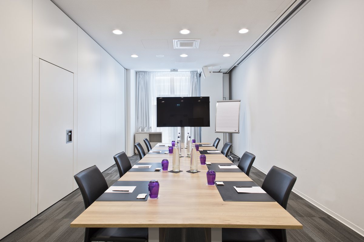 Heller Besprechungsraum mit langem Holztisch, Bildschirm und Flipchart, vorbereitet für einen Workshop